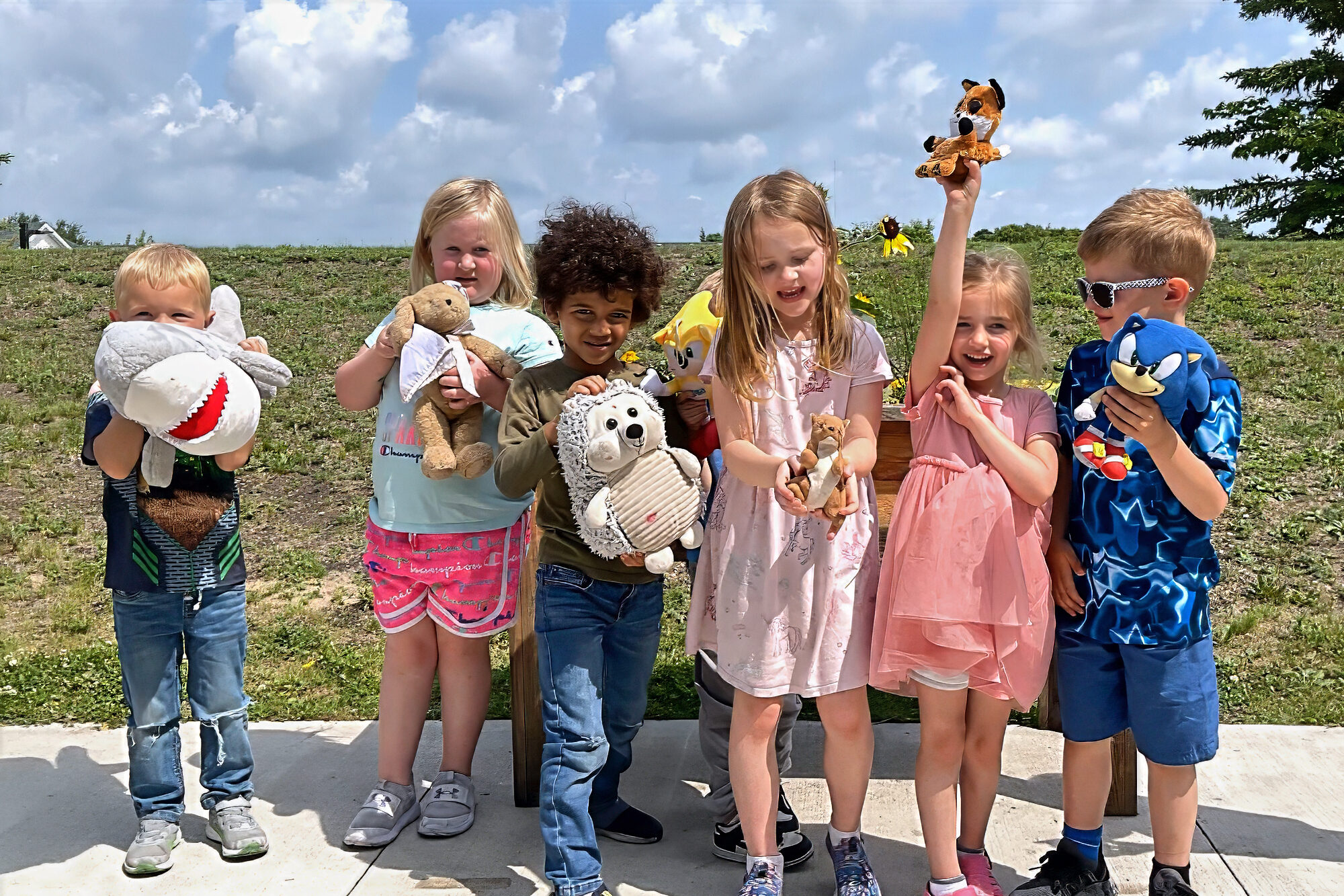 Preschool kids holding stuffed animals outside on a sunny day
