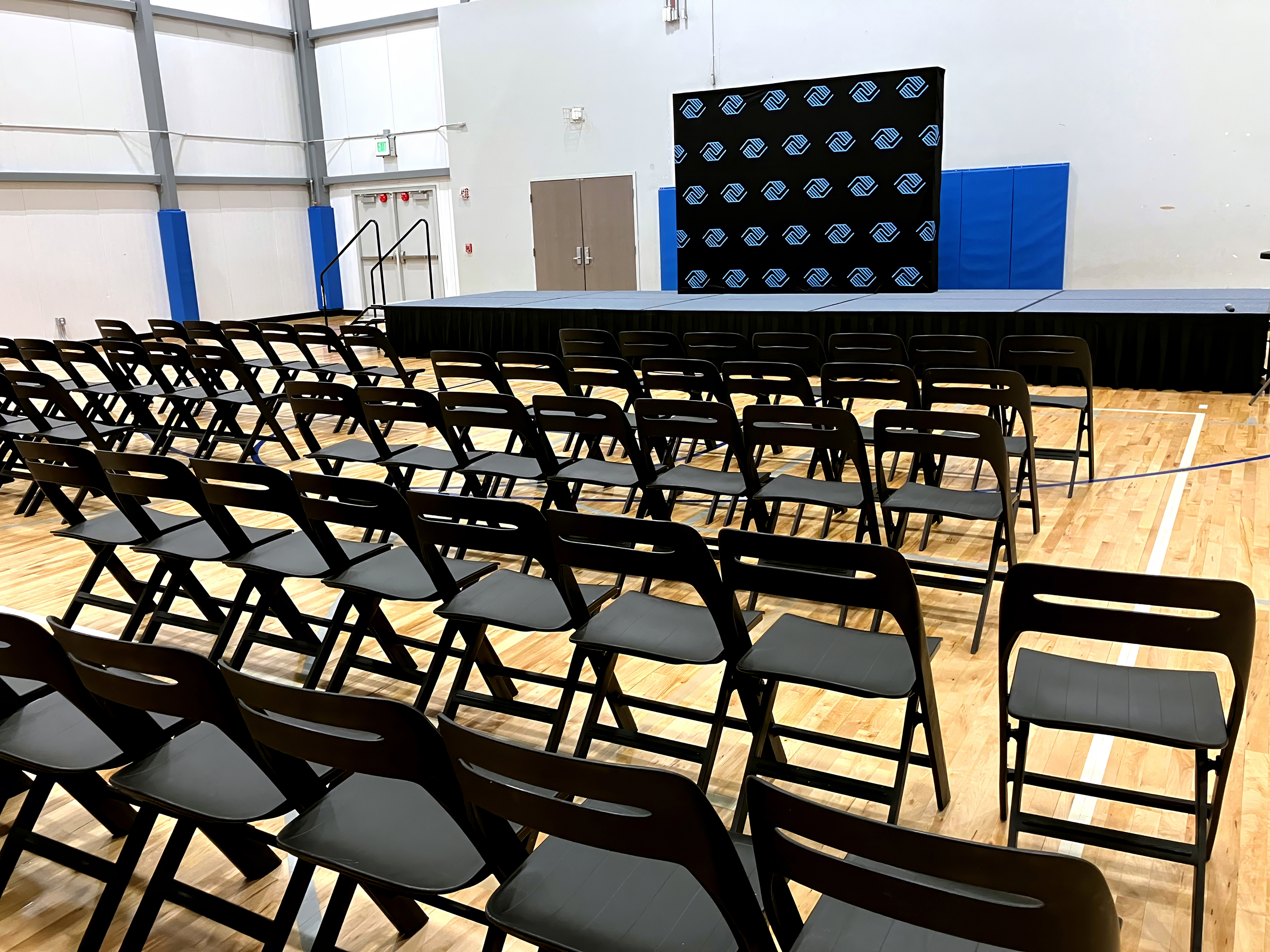 Rental Space • Gymnasium • featuring stage with step & repeat background and 75 chairs on the floor space