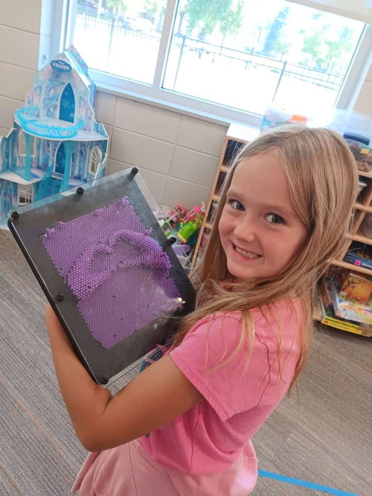 Smiling girl holding a purple hand-shaping toy frame