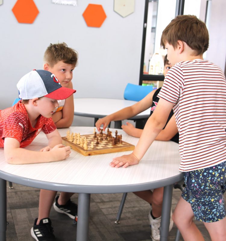 grade school boys play chess at a table