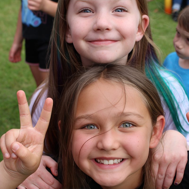 two smiling girls showing the peace sign with their fingers