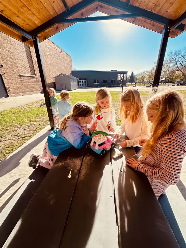 a group of girls outside in working on an activity at a picnic table.